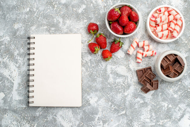 冬青顶视图碗与草莓巧克力糖果和一些草莓巧克力糖果在右侧和一个笔记本在灰白色的桌子左侧巧克力糖果壁板