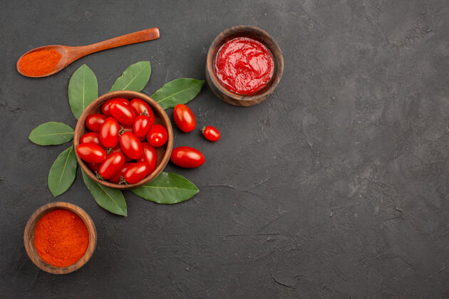 勺子顶视图一碗樱桃西红柿在黑桌子上留下一个木勺和几碗番茄酱和辣椒粉浆果蔬菜黑