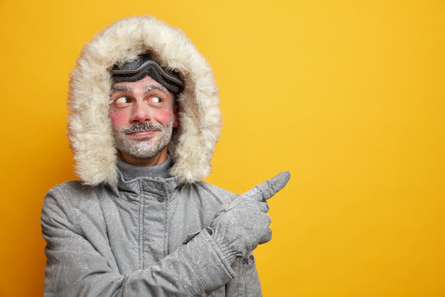 度假高兴的未刮胡子的欧洲男子建议参加滑雪比赛穿灰色外套点在复制空间男性黄色手套