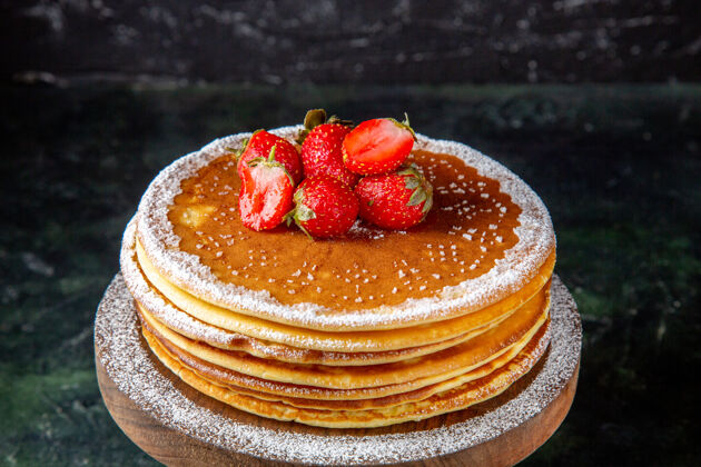正面正面是美味的蜂蜜蛋糕和新鲜的草莓放在黑色的圆木板上甜点糖板