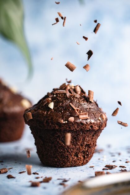 棕色垂直选择焦点拍摄巧克力杯形蛋糕在一个蓝色的表面与巧克力碎片下降蛋糕糖美味