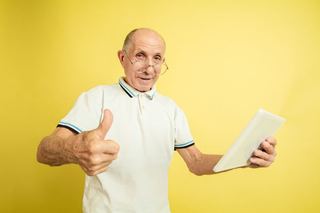 健康使用平板电脑 竖起大拇指黄色工作室背景上的高加索老人肖像美丽的男性情感模型人类情感的概念 面部表情 销售 福利 广告空间成功英俊高管