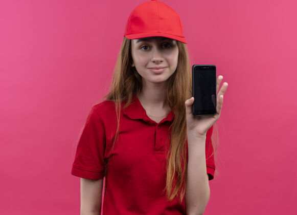 送货一个穿着红色制服 拿着手机的年轻送货女孩高兴地站在孤立的粉色空间里女孩年轻制服