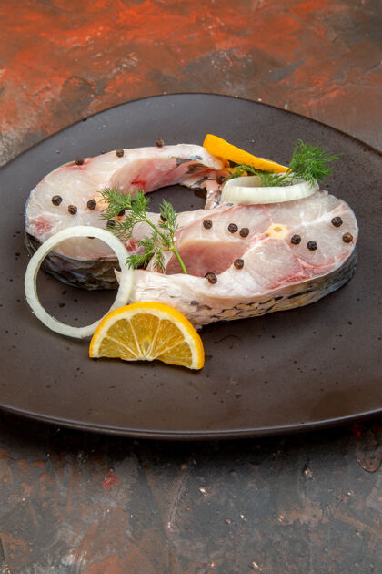 晚餐生鱼片和胡椒柠檬片洋葱的垂直视图在混合色表面的黑色盘子上混合餐厅生鱼