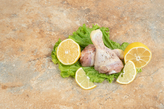 生的生鸡腿配柠檬片和生菜放在大理石表面美味食物配料
