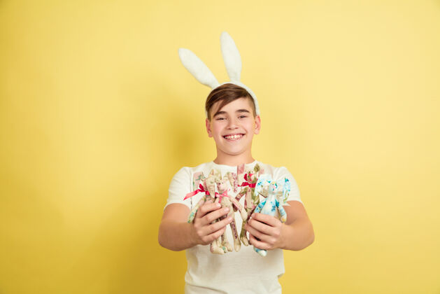 帅气快乐装饰白人男孩作为一个复活节兔子在黄色的工作室背景复活节快乐的问候美丽的男模人类情感的概念 面部表情 节日复制空间强壮创意搞笑