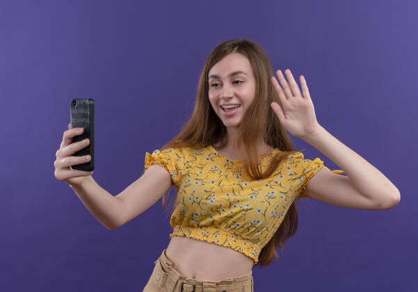 你好快乐的年轻女孩拿着手机 在孤立的紫色空间里对着手机打招呼手势年轻电话