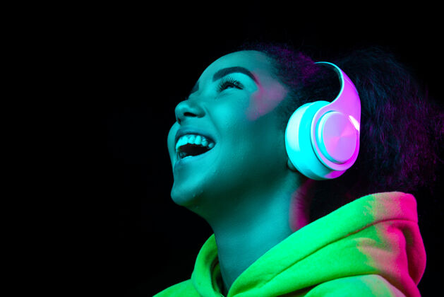 音乐耳机在五彩霓虹灯下的黑暗工作室背景上孤立的非洲裔美国女性肖像美丽的女性模特人类情感的概念 面部表情 销售 广告 时尚成功脸移动