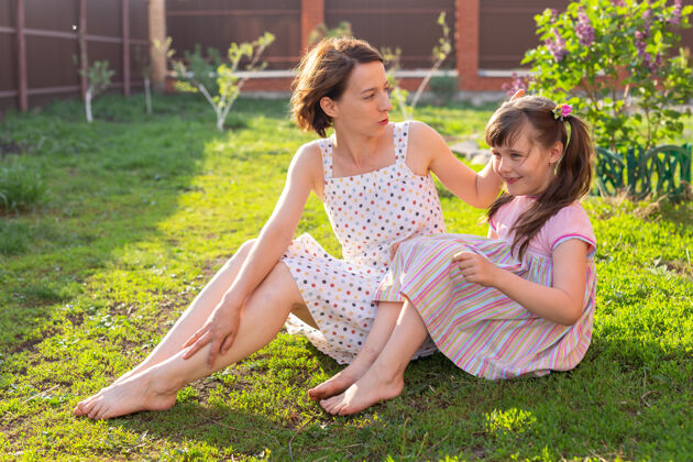 乐趣穿着粉红色衣服的小女孩和她妈妈在院子里坐在草地上夏天衣服漂亮