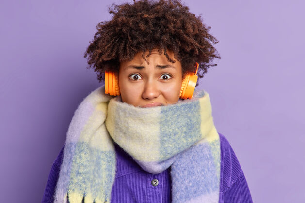 季节特写镜头不高兴的非洲裔美国女性因寒冷而发抖脖子上戴着暖和的围巾在冬天花了很多时间在外面通过耳机听音频紫色音乐休闲