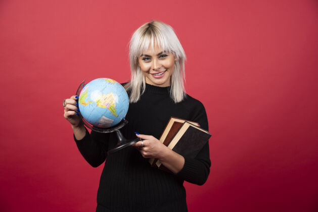 姿势年轻的女模特在红墙上摆着一本书和一个地球仪肖像教科书书房
