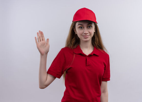 年轻穿着红色制服的自信的年轻送货女孩在与世隔绝的空白处打招呼红色你好手势