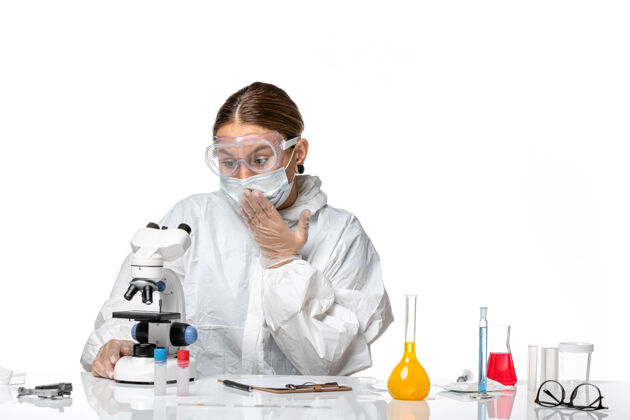 视野前视图女医生穿着特制的工作服 戴着口罩 在显微镜下观察白色背景的冠状病毒大流行病毒外套套装