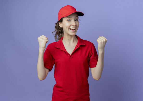 手势快乐的年轻漂亮的送货女孩 穿着红色制服 戴着帽子 在紫色背景上做着“是”的手势 并留有复印空间女孩背景交付