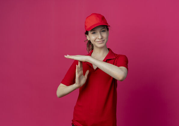 红色令人高兴的年轻漂亮的送货女孩 穿着红色制服 戴着帽子 在深红色的背景下与复制空间隔离年轻手势帽子