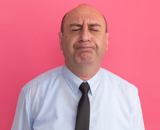人关注闭着眼睛的中年男子穿着白色t恤 领带隔离在粉红色的墙上人人表情