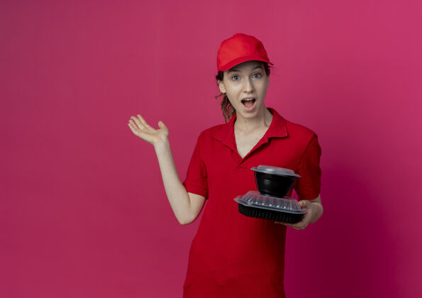 红色令人印象深刻的年轻漂亮的送货女孩穿着红色制服和帽子举行食品容器显示空的手在深红色背景与复制空间隔离持有漂亮帽子