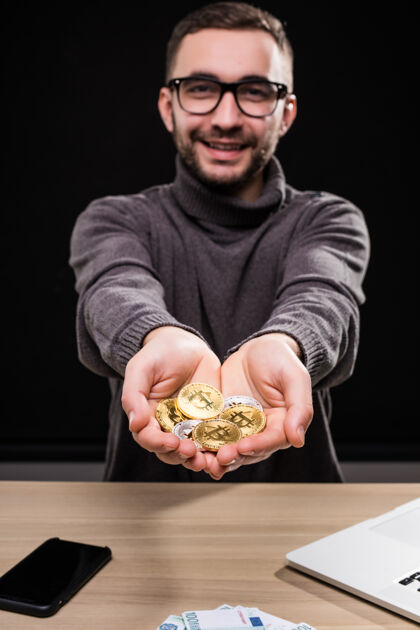 数据戴眼镜的人的画像 在桌子上 他手里拿着金色的比特币 与黑色隔在一起金融硬币加密货币