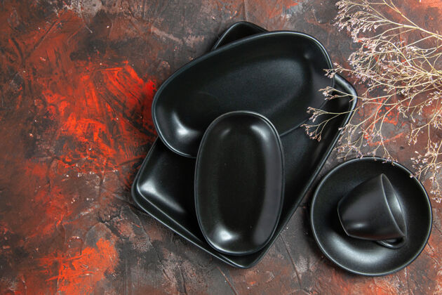 深色黑色椭圆形和矩形盘子的顶视图暗红色表面上的黑色杯子和碟子电子设备鼠标碟子