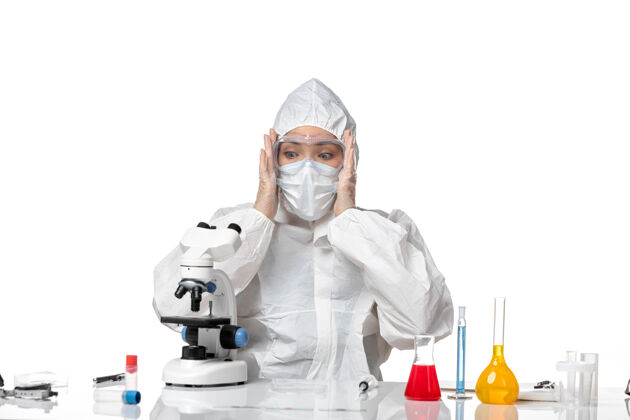 大流行正面图女医生穿着防护服戴着口罩由于害怕用显微镜观察白色背景病毒大流行溅起的covid-专业视野药品