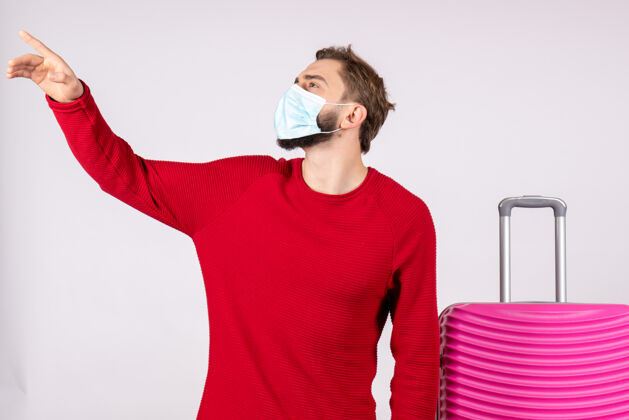 游客正面图白色墙壁上戴着粉红色面具的年轻男性航程病毒-飞行旅行假期情感病毒飞行病毒年轻男性