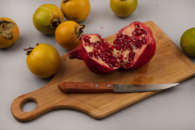 水果木制菜板上的石榴被切成两半 上面夹着一把柿子水果刀刀多汁木材