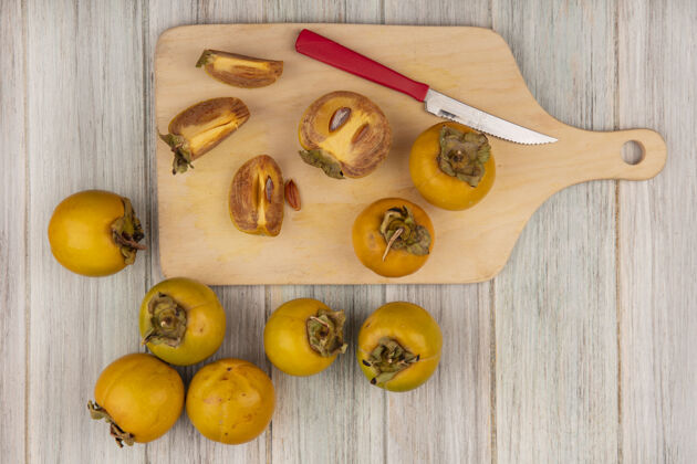 板黄色柿子水果的顶视图在一个木制的厨房板上 在灰色的木制桌子上放着一把刀灰色刀橘子