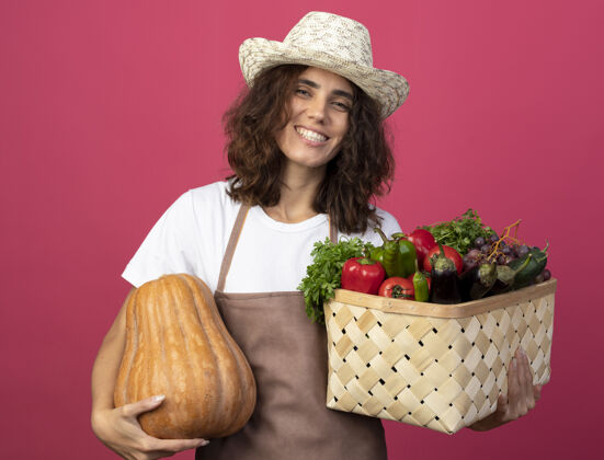 篮子年轻的女园丁面带微笑 穿着制服 戴着园艺帽 手里拿着一个蔬菜篮子 篮子里的南瓜是粉红色的南瓜穿年轻人