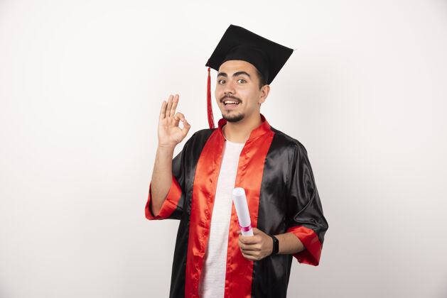 帽子快乐的男生拿着文凭在白色上做ok标志毕业年轻男性
