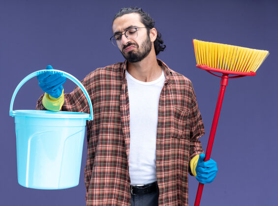 帅气年轻帅气的清洁工 穿着t恤 戴着手套 拿着一个桶 把拖把隔在蓝色的墙上年轻清洁举行