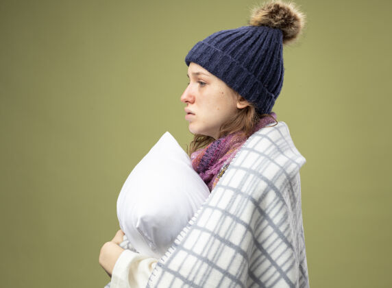 站站在侧视图年轻的生病的女孩穿着白色长袍和冬季帽子围巾包裹在格子抱枕侧写长袍年轻人