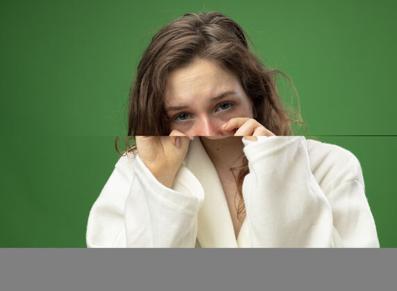 疾病哭泣的年轻病女孩穿着白色长袍擦眼睛与双手隔离在绿色哭泣年轻眼睛