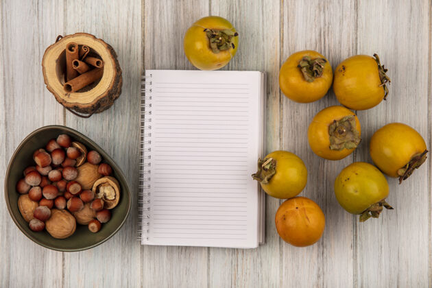 食物黄色柿子水果与榛子和核桃的顶视图在一个灰色的木制桌子上的一个碗与复制空间榛子核桃顶部
