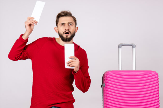 风景正面图：年轻男性 带着粉色包 手持白墙旅行的机票 彩色度假航班 夏季旅游者肖像度假颜色