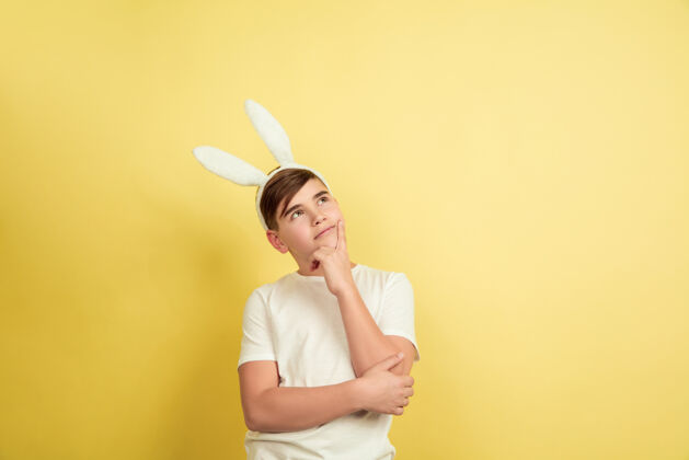 青少年体贴 梦想白人男孩作为一个复活节兔子在黄色的工作室背景复活节快乐的问候美丽的男模人类情感的概念 面部表情 假期复制空间有趣庆典男性