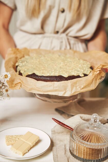 女性年轻的女厨师在白色的桌子上做着美味的奶油巧克力蛋糕霜糕点糖