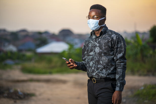新年轻的非洲裔美国男性戴着防护面罩在户外使用手机成人流行病医疗