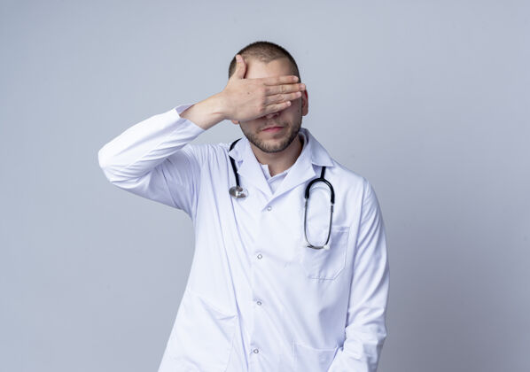 围着年轻的男医生穿着医用长袍 脖子上戴着听诊器 闭上眼睛 手被隔离在白色背景上 留有复印空间医生闭着长袍