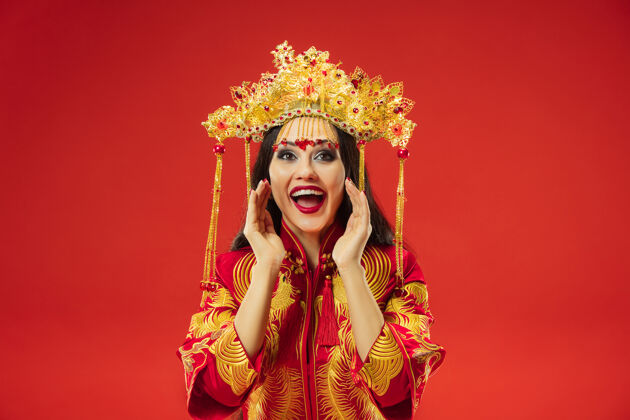 脸中国传统的优雅女子在摄影棚的红色背景美丽的女孩穿着民族服装中国新年 优雅 优雅 表演者 表演 舞蹈 女演员 服装的概念尖叫惊讶亚洲