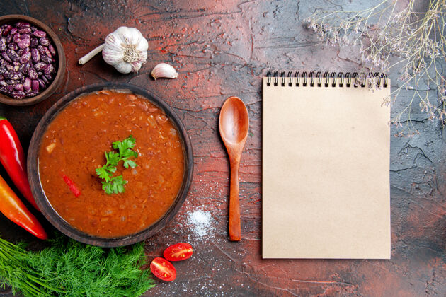 勺子番茄汤在一个棕色的碗和不同的香料大蒜柠檬和笔记本上混合的颜色表碗笔记本食物
