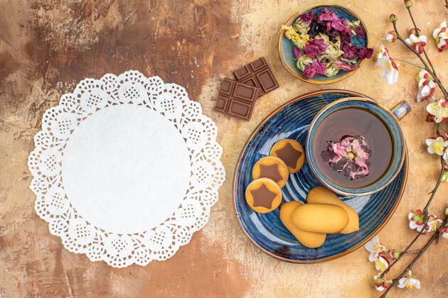 陶瓷器皿上图各种饼干一杯茶和鲜花巧克力条放在五颜六色的桌子上治疗食品鲜花