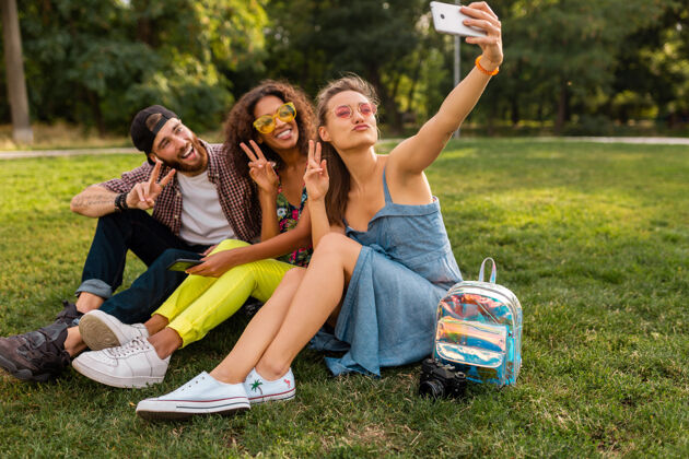 人五彩缤纷时尚快乐的年轻朋友陪伴坐在公园里 男女同乐青春女人团体