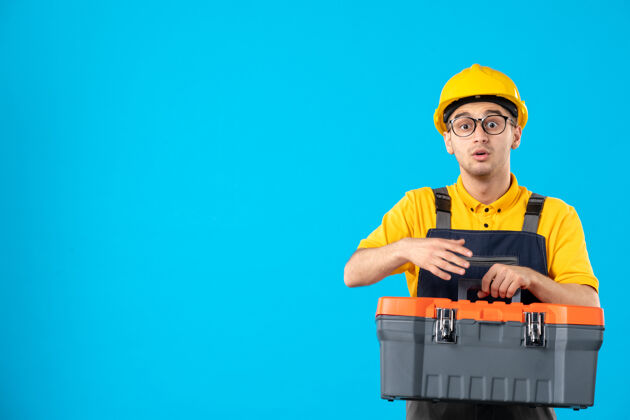 手前视图的男性建筑工人在制服与工具箱在他手中的蓝色墙上制服杂工水管工
