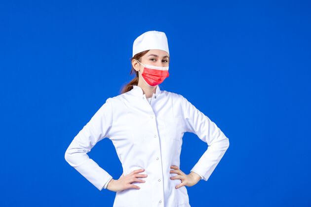 医疗正面图身着医疗服的年轻护士 蓝色墙上戴着红色防护面具成人防护套装