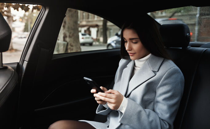 旅程坐在后座上开车旅行的女商人 在会议上开车时通过智能手机阅读短信年轻旅游一