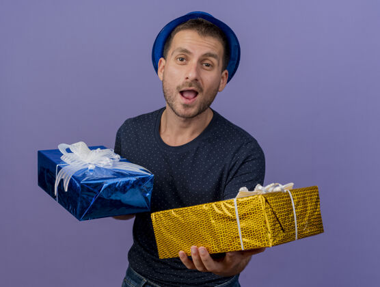 紫色快乐英俊的白人男子戴着蓝色的帽子拿着礼品盒孤立的紫色背景与复制空间欢乐空间复制