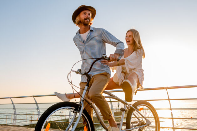 情感骑自行车旅行的年轻帅哥美女 夏日夕阳海边的浪漫情侣 波西米亚时尚装扮 朋友们在一起玩得开心旅行者日落浪漫