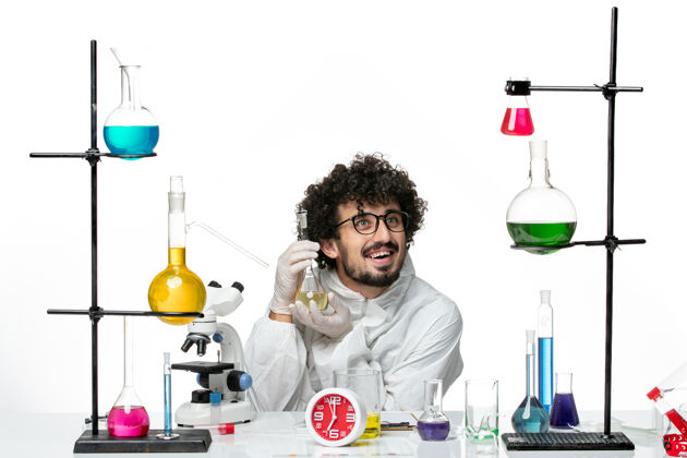 视图正面图：年轻的男科学家穿着特制的衣服 拿着白墙上的装有溶液的烧瓶溶液烧杯化学