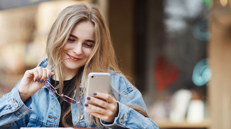青年快乐的女人在街上的快餐店用智能手机 微笑着w中国人窗户女孩