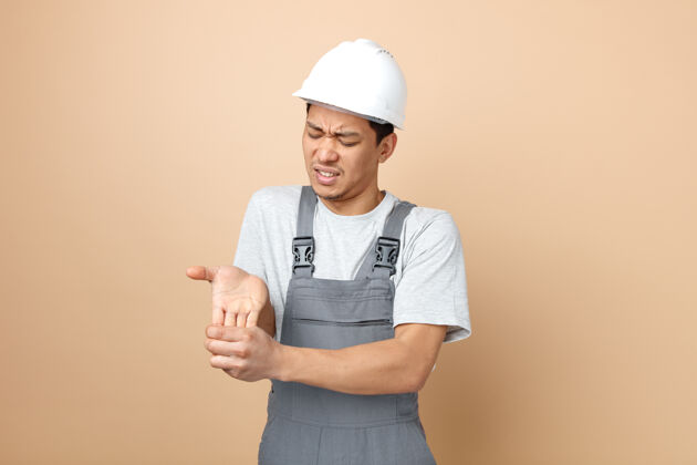 头盔戴着安全帽和制服的年轻建筑工人 双手紧闭双眼 疼痛难忍手安全奶油